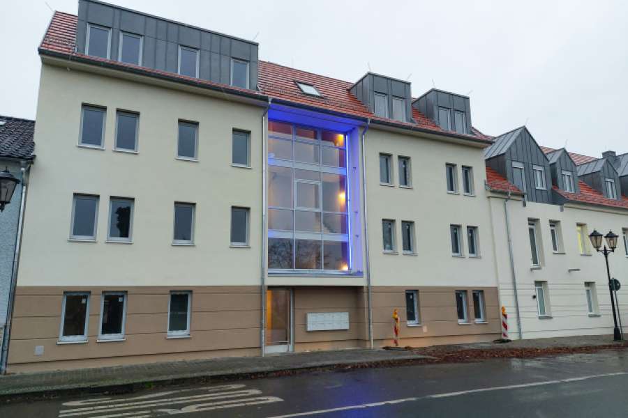 Gebäudefassade des Wohnprojektes „Alte Brauerei“ der WIS Wohnungsbaugesellschaft im Spreewald mbH in Altdöbern, gegenüber der Kirche. Ein großes Panoramafenster im Neubau wirkt modern. BILD: WIS Wohnungsbaugesellschaft im Spreewald GmbH 