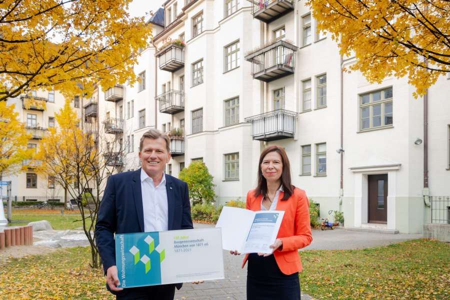 Verbandsdirektor Hans Maier übergibt ein Jubiläumsschild der Wohnungswirtschaft an Vorstand Sandra Marko. Foto: VdW Bayern/Andreas Heddergott